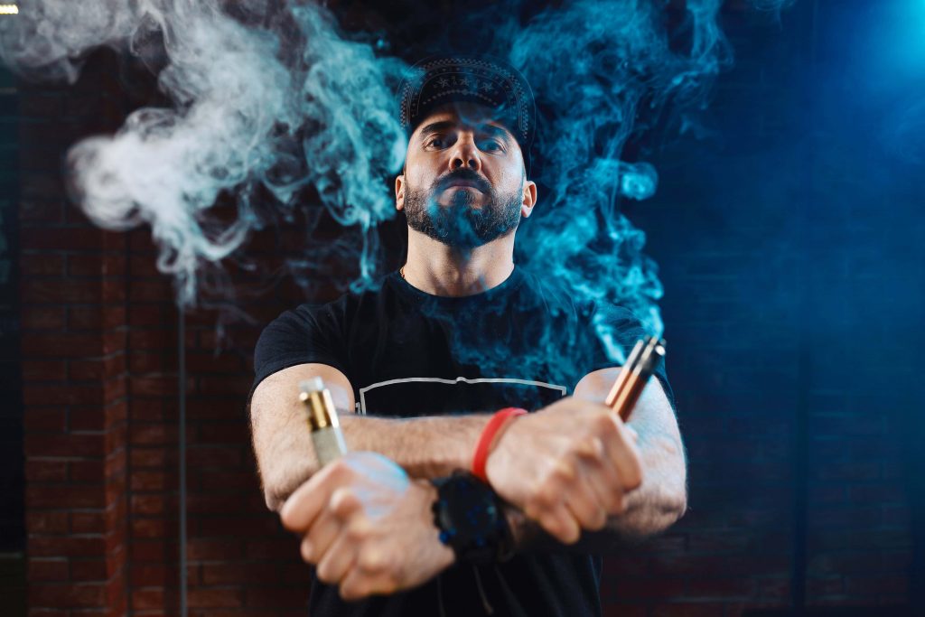 Dispositivo de vape con vaporizador y humo, hombre vapeando en tienda de cigarrillos electrónicos.