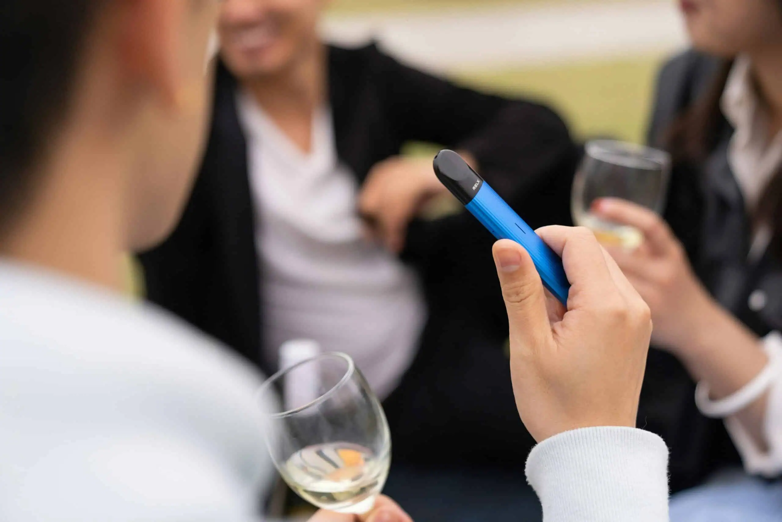 Batería de vape azul con Wi-Fi en manos de mujer en reunión social con copas de vino.